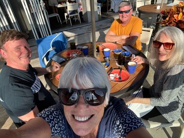 Group selfie of four friends enjoying a sunny outdoor meal.