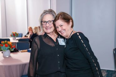 Two women smiling and posing together at an indoor event.