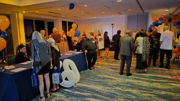 People gathered at a decorated indoor event with balloons and tables.