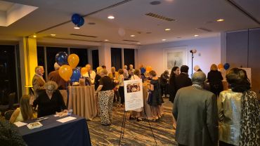 People mingling at an indoor event with orange and blue balloons.