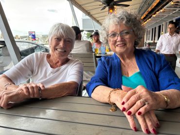 Two elderly women sitting and smiling at an outdoor restaurant.