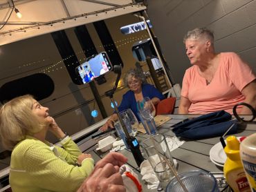 Three elderly women enjoying a lively conversation around an outdoor table at night.