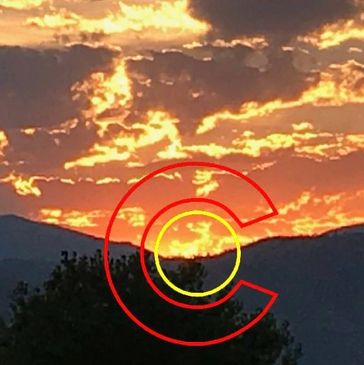 Sunset over mountains with dramatic clouds and silhouetted trees.