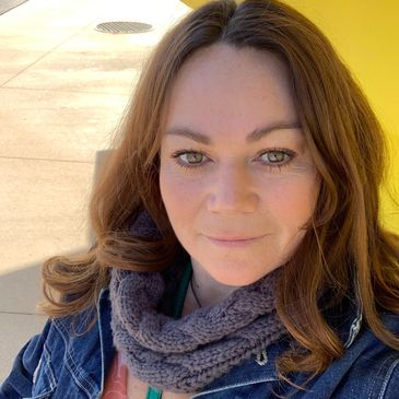 A woman with green eyes wearing a denim jacket and knitted scarf outdoors.