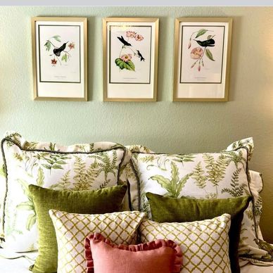Decorative pillows with botanical prints and framed bird art above a bed.