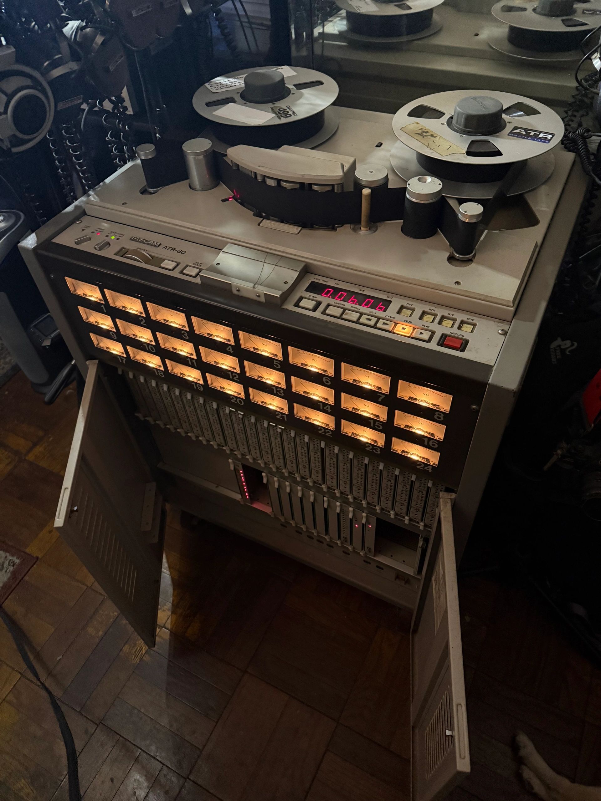 Vintage Tascam ATR-80 reel-to-reel tape recorder with illuminated meters and open cabinet doors.