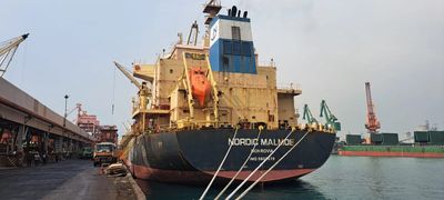Large cargo ship docked at a busy port with cranes and vehicles nearby.