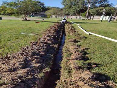 A trench dug in a grassy area with a person working at the far end.