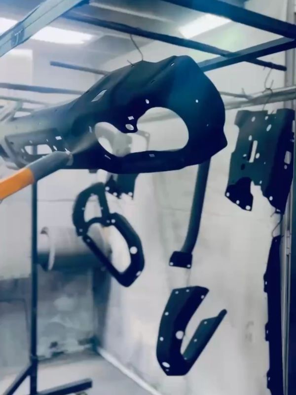 Black metal parts hanging in a factory setting.