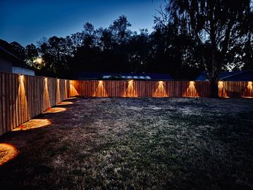 Backyard fence lights illuminating grass at night.