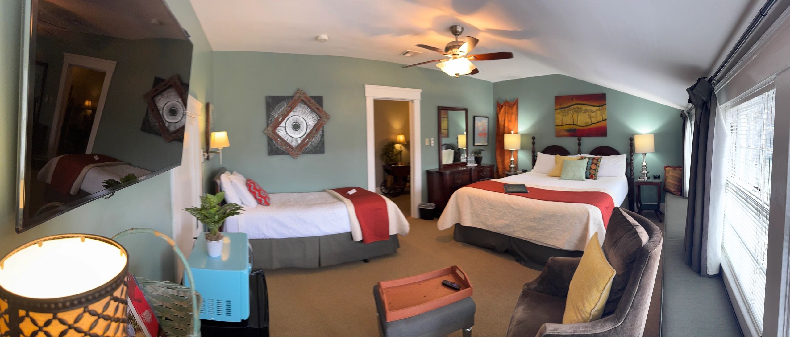 A wide-angle view of a hotel room with two beds, a chair, and a mirror.