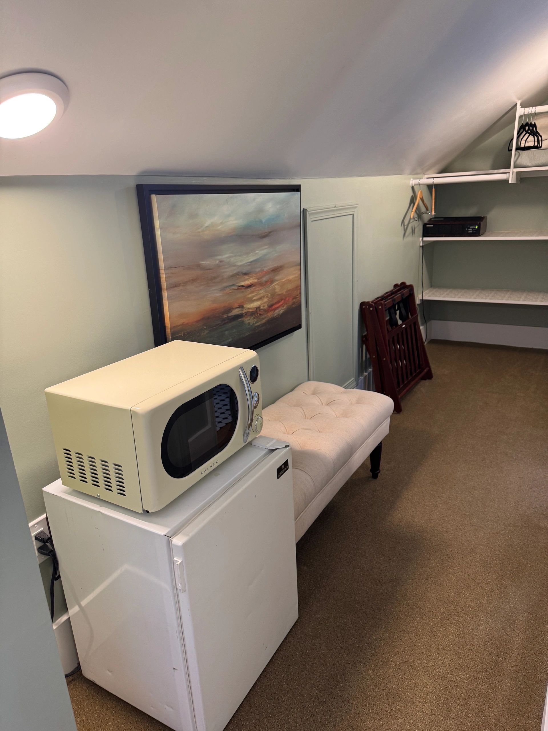 A small room with a microwave and mini fridge on a bench and shelves.