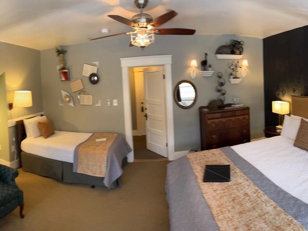A wide view of a room with two beds, a doorway, and a ceiling fan.