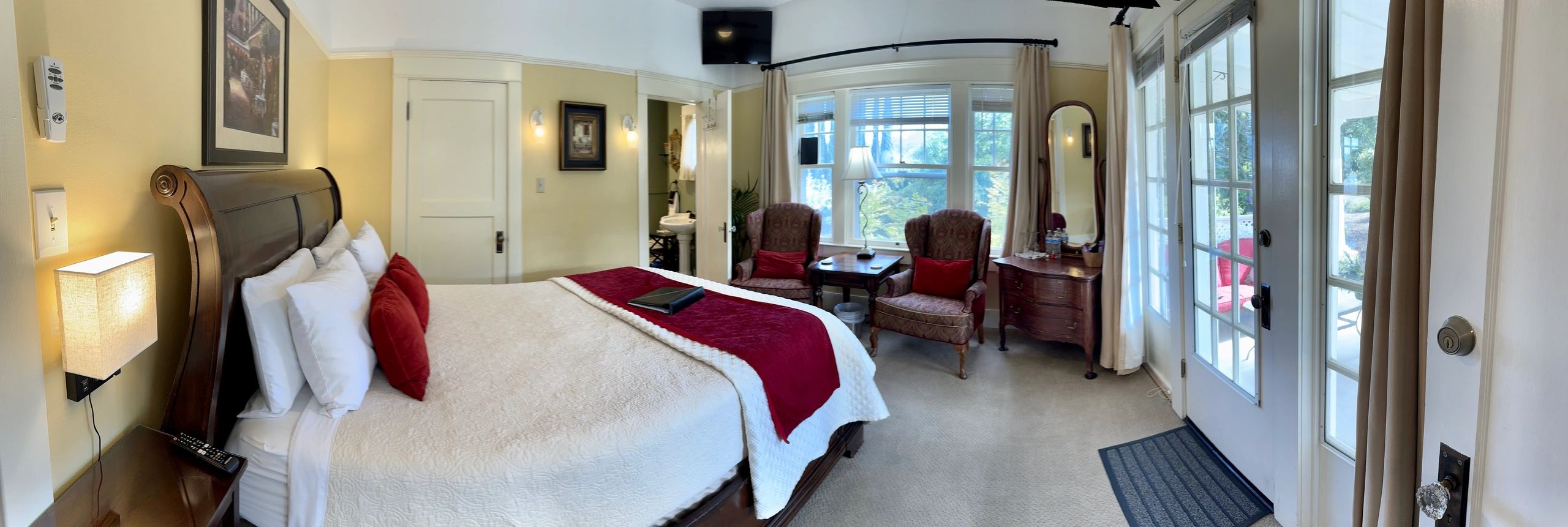 A wide-angle view of a hotel room with a king-sized bed, two reading chairs, and a window with a view.