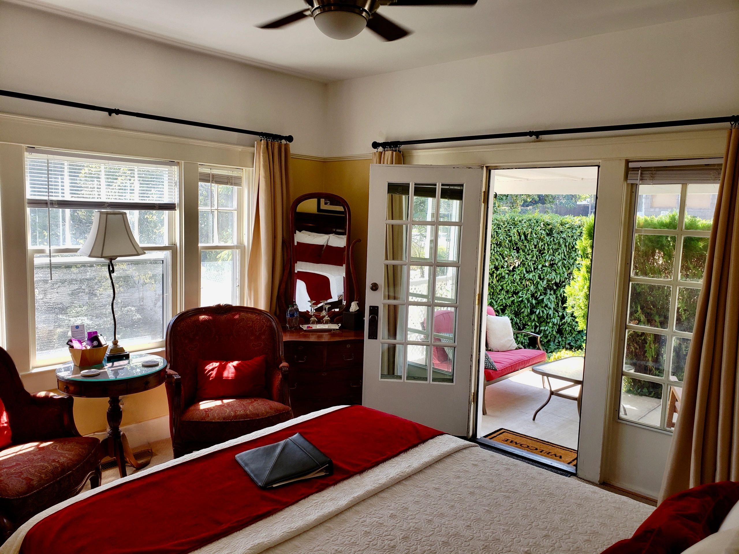 A hotel room with a red bedspread, white quilt, and red armchair.