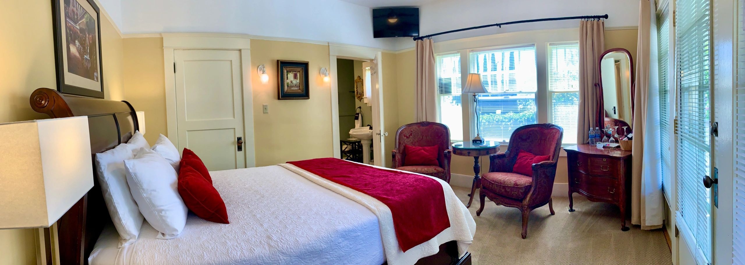 A hotel room with a bed, two red chairs, a window, and a TV.