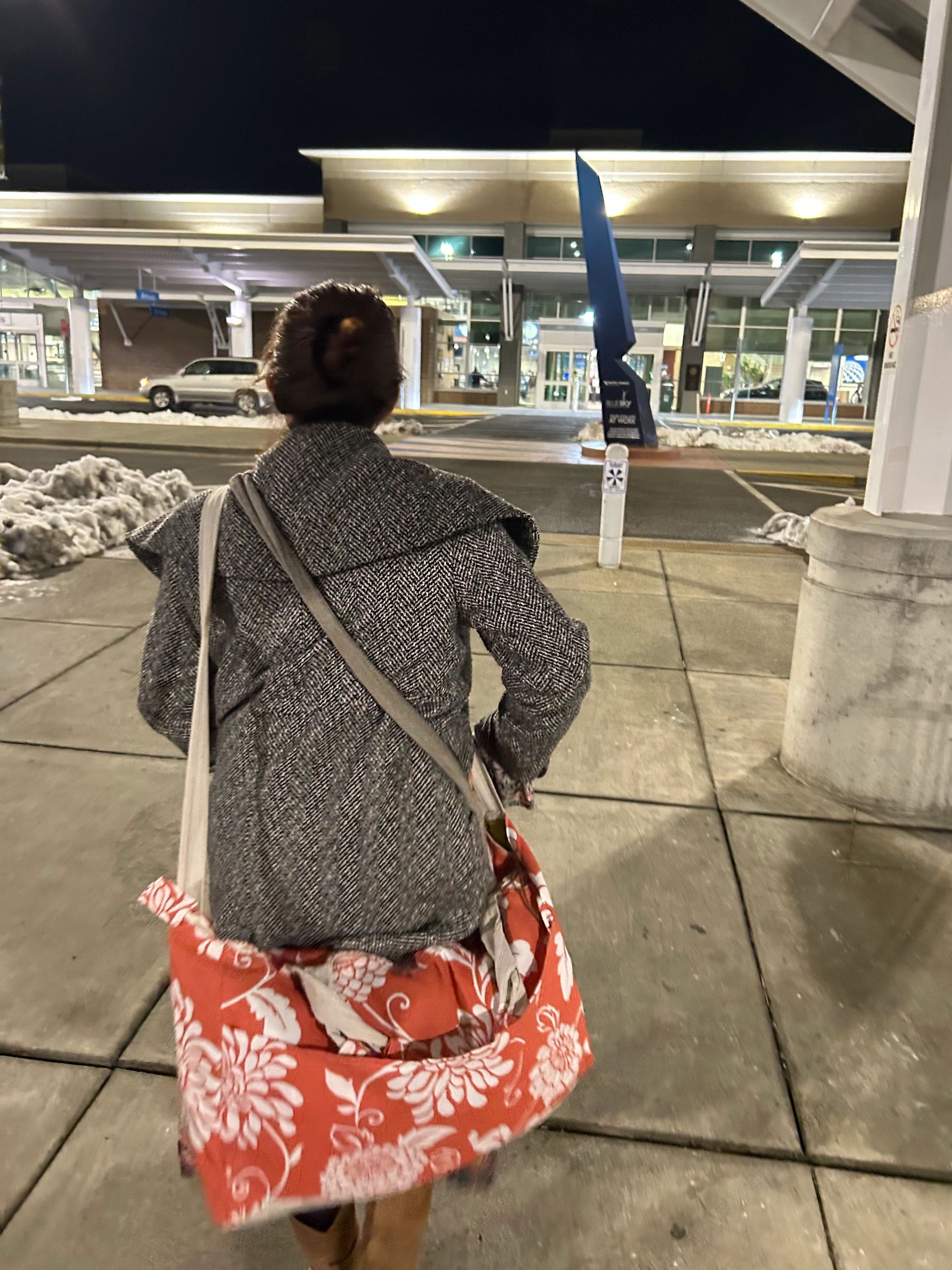 A nighttime view of a building's exterior with a canopy and a person walking in front.