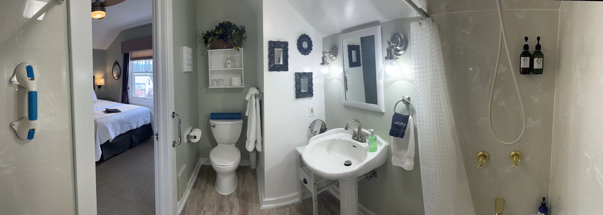 A panoramic view of a bathroom with a shower, sink, toilet, and towels, with a doorway leading to a bedroom.