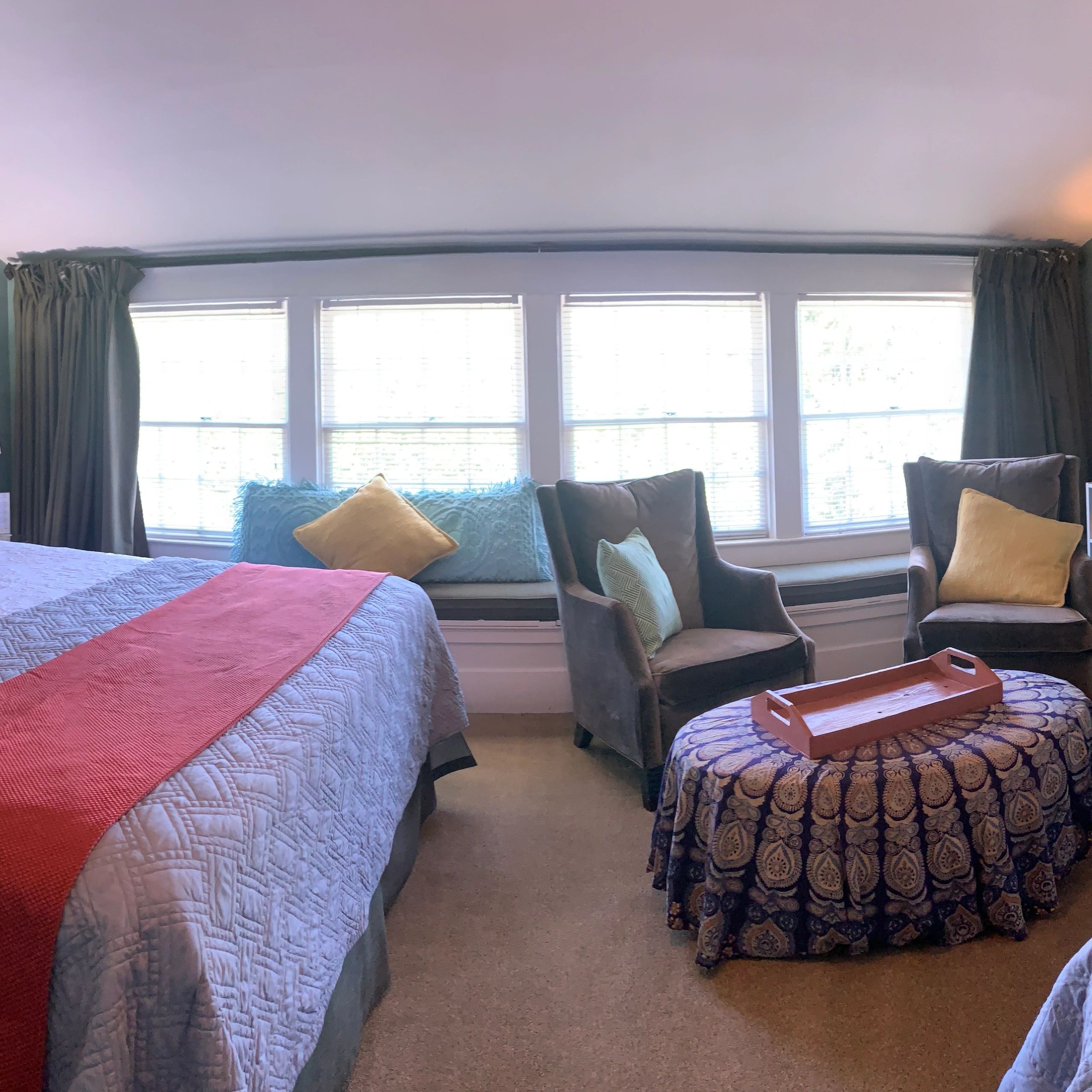 A wide view of a hotel room with a bed, two chairs, a table, and a window with curtains.