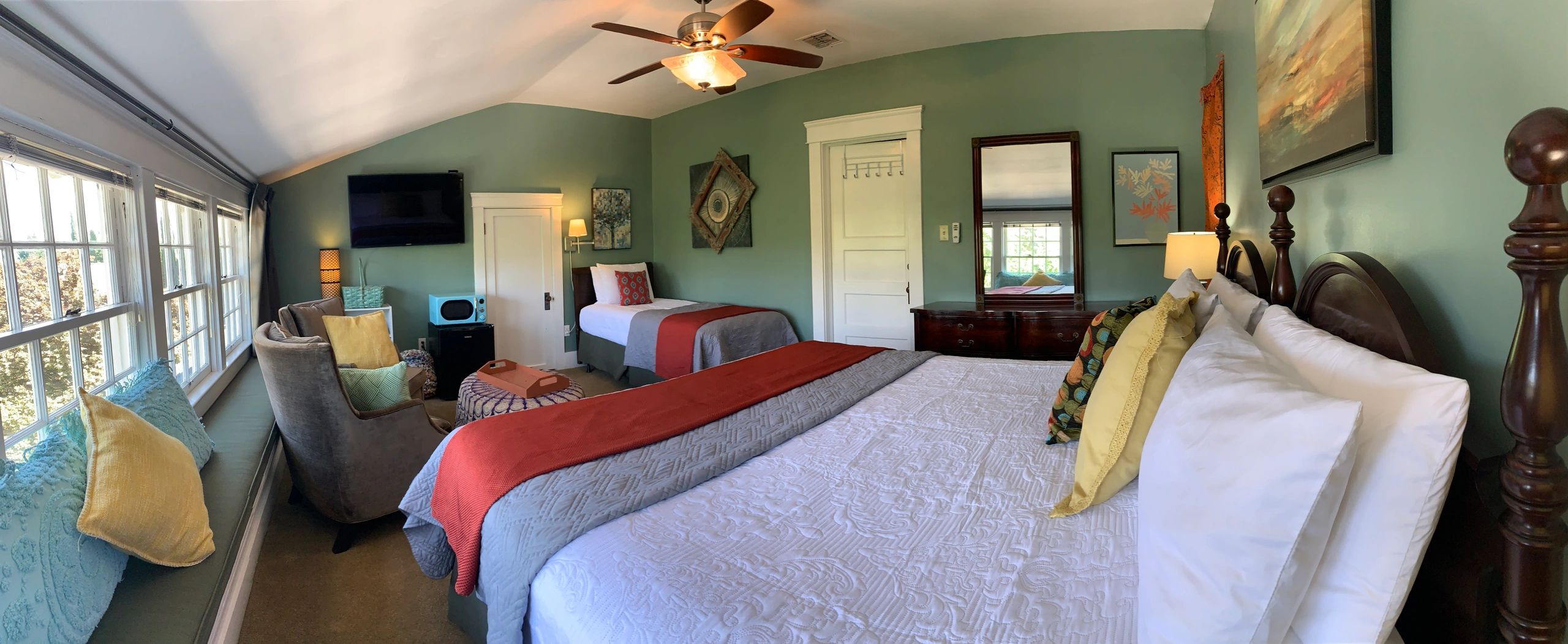 A wide-angle view of a hotel room with two beds, a sofa, and a TV.