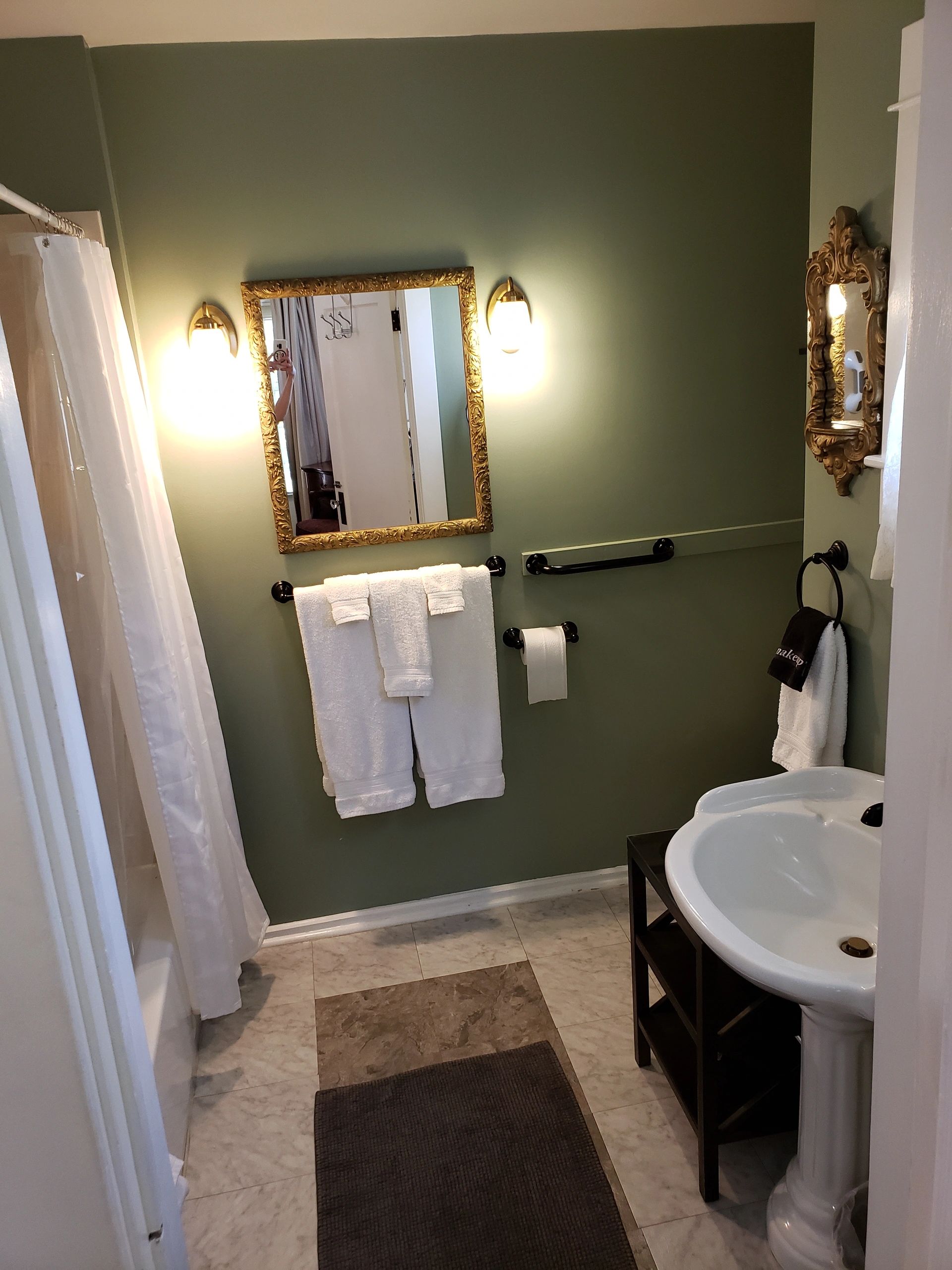 A bathroom with a white sink, gold-framed mirror, and shower curtain.