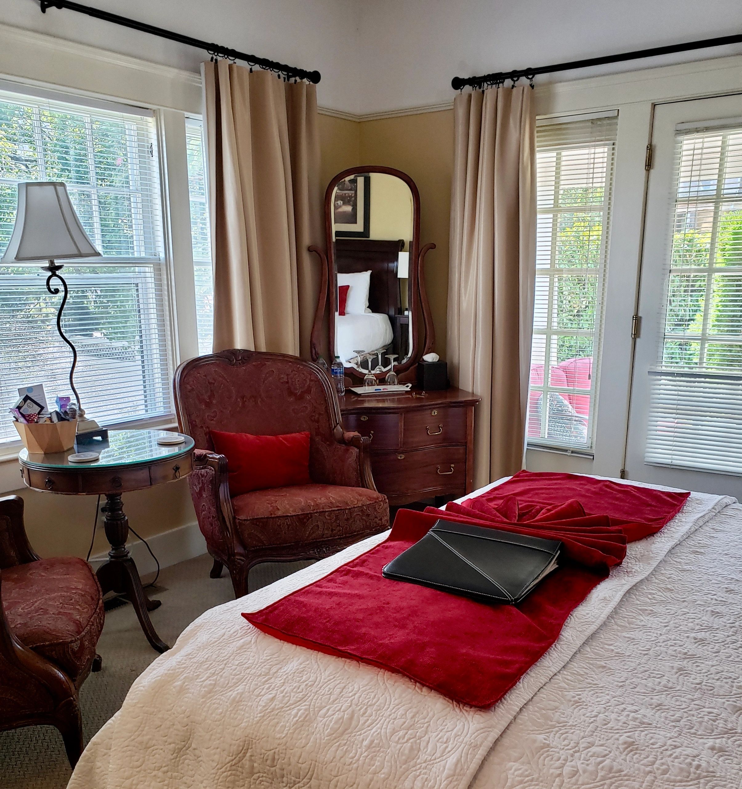 A hotel room with a bed, chair, window, mirror, and dresser.