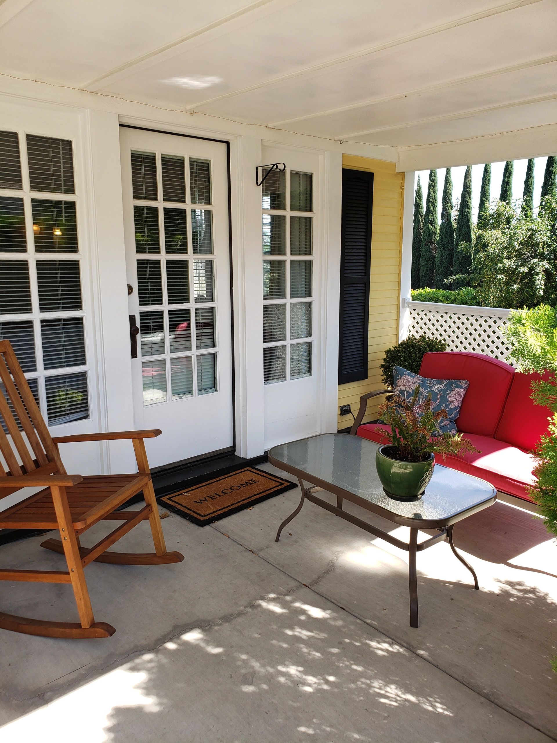 A cozy porch with a red couch, wooden rocking chair, and glass-top table.