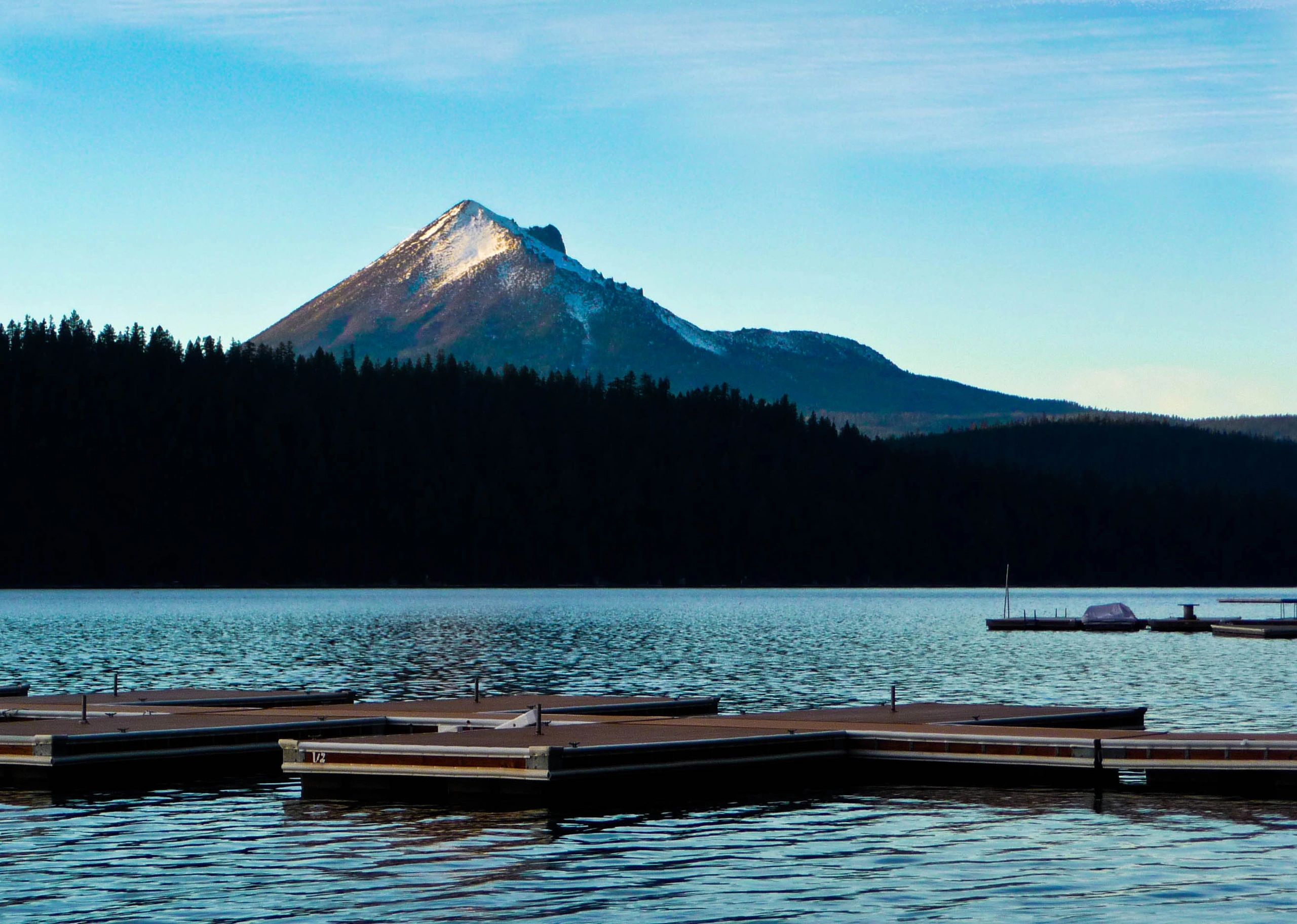 A serene lake scene with a dock in the foreground and a snow-capped mountain in the background.