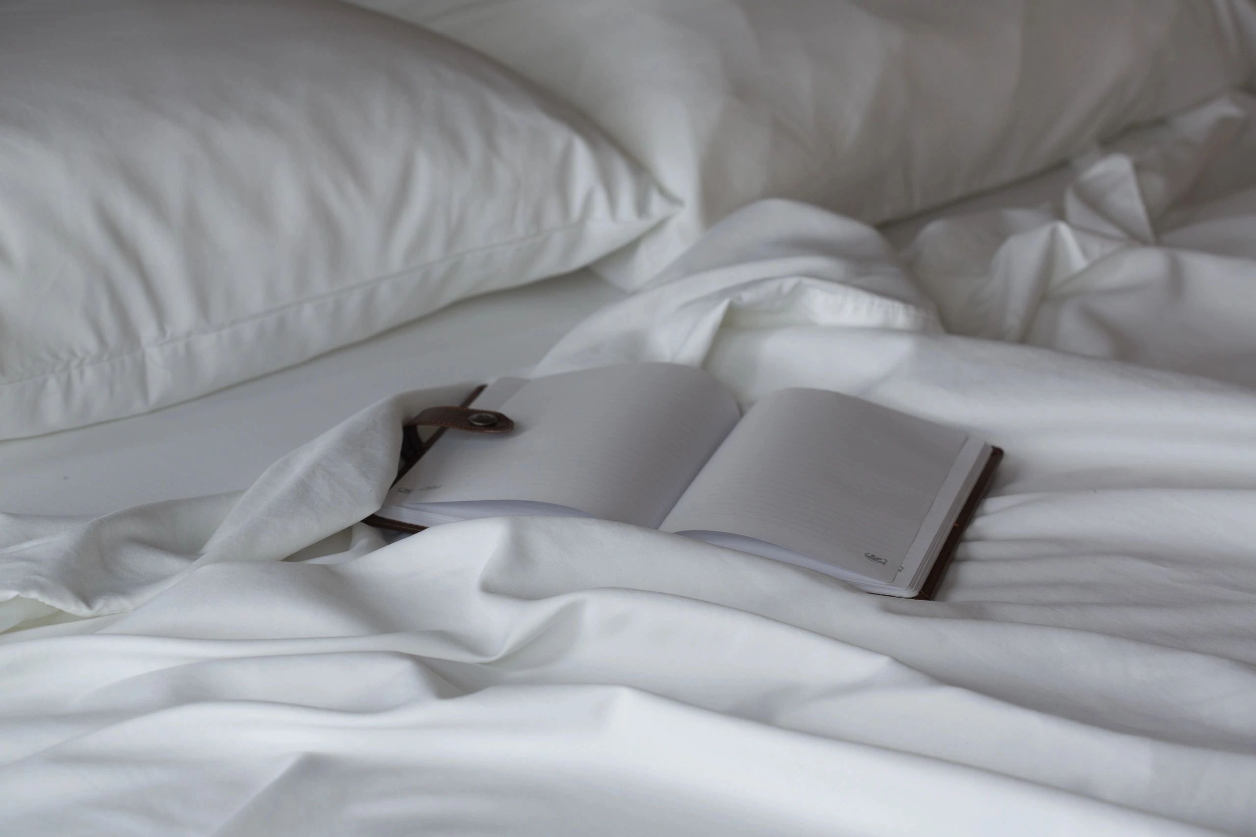 A bed with white linens and an open book on top.