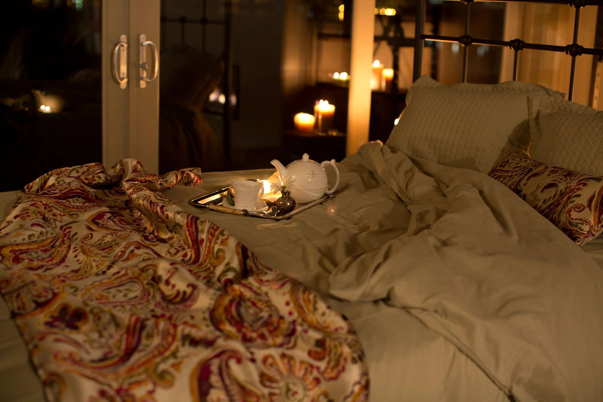 A bed with a tea tray on it and candles in the background
