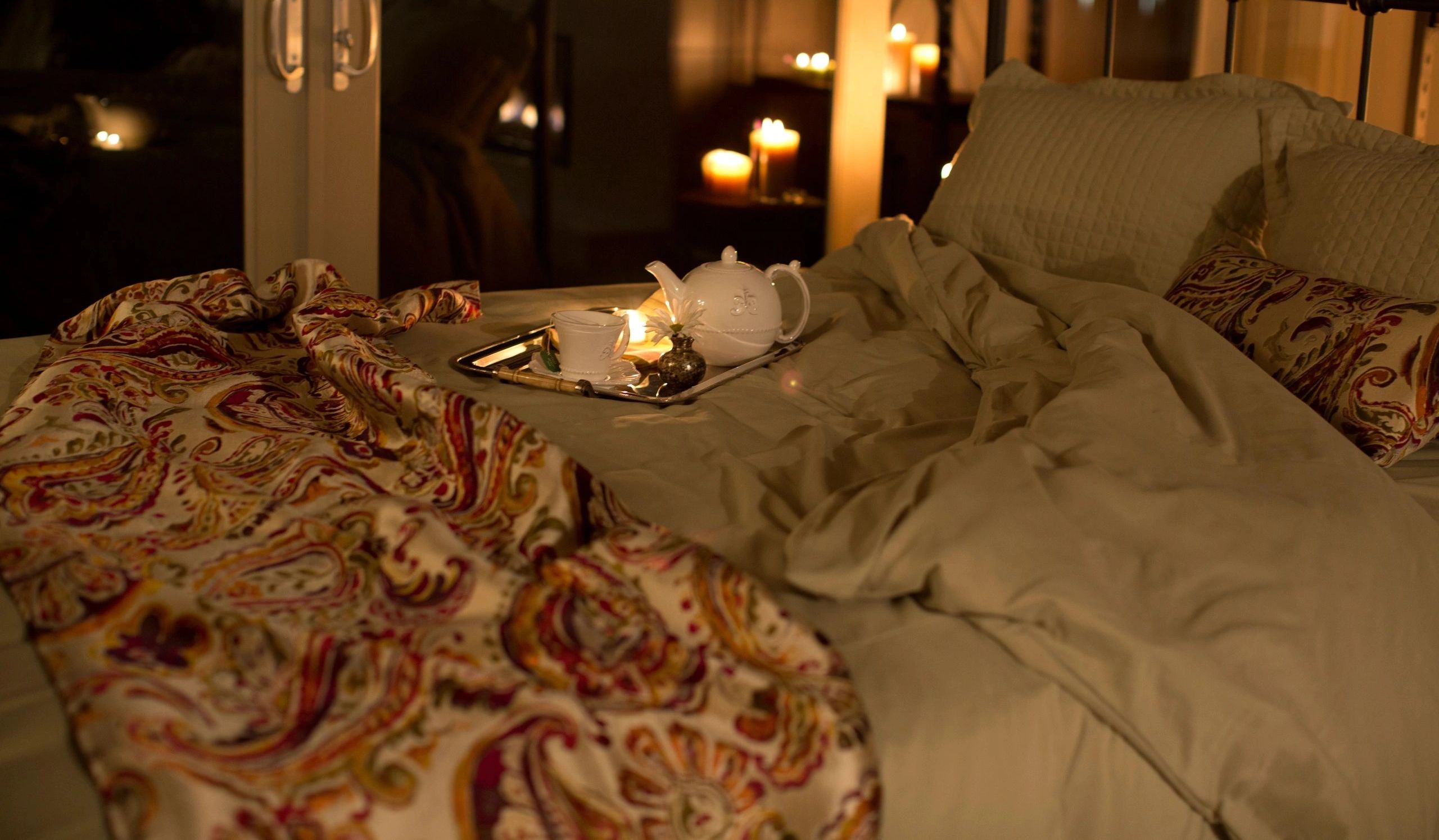 a bed with a tea tray, candles, and a paisley comforter