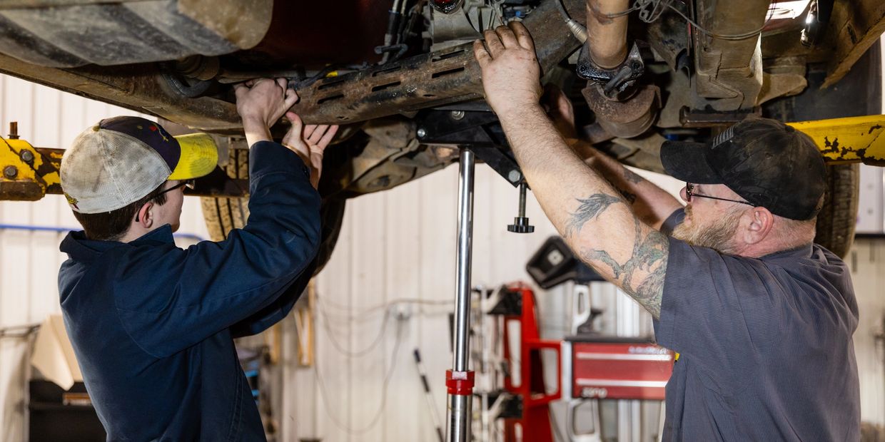 Two workers are working on a car to repair