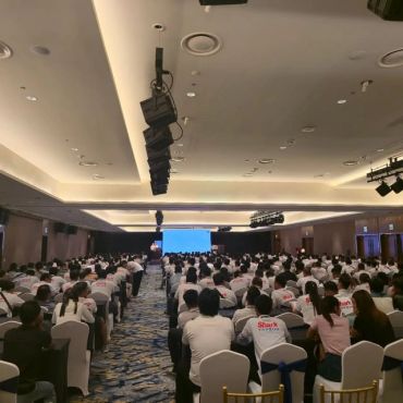 Large conference room filled with attendees in white shirts.