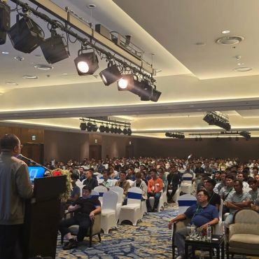 Speaker addressing a large audience in a conference room.