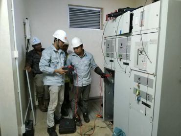 Electricians inspecting a control panel wearing safety helmets.