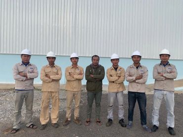 Group of seven men posing outdoors with safety helmets.