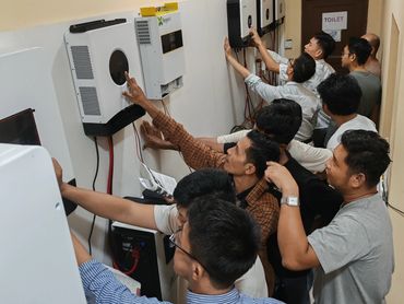 Group of men examining wall-mounted electronic devices.