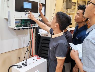 Men inspecting a white electronic device mounted on a wall.