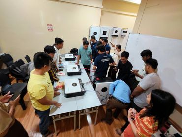 Group of people around electronic devices in a workshop.