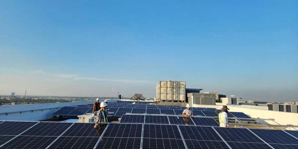 Engineers inspecting rooftop solar panels under clear blue sky.