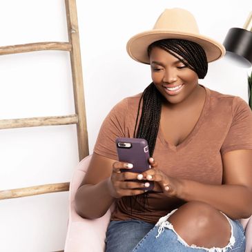 African American woman sitting in a chai dressed in a tan hat, brown shirt, and denim ripped jeans. 