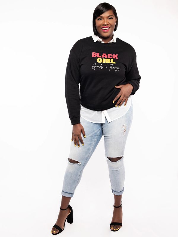 African American woman standing with a black crew neck sweater with writings.
