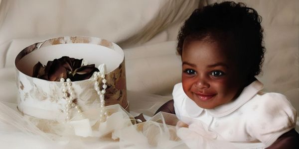Smiling baby girl with a pearl necklace and gift box.