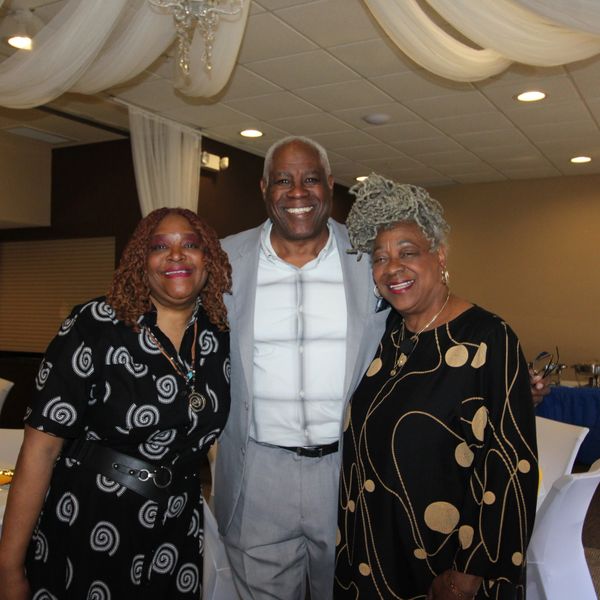 Three adults smiling together at an indoor event with elegant decor.