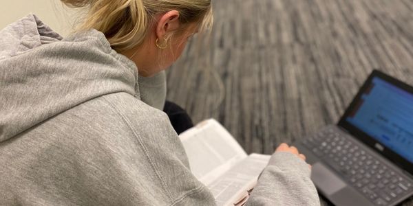 Person reading a book with a laptop nearby.