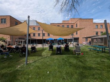 Group of elderly people in wheelchairs outdoors with tents.