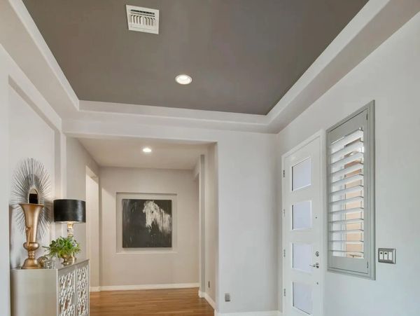 Modern hallway with recessed ceiling, wooden floor, and white entrance door.