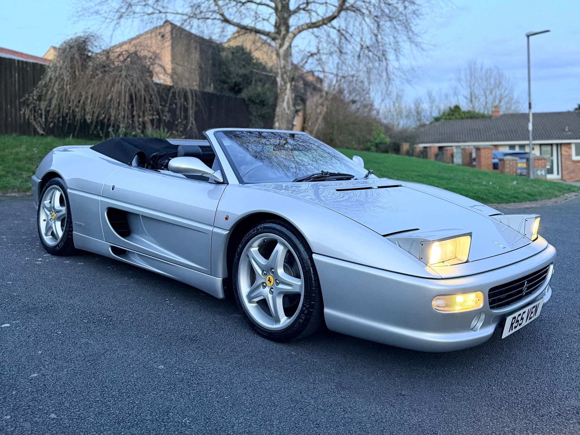Silver Ferrari convertible with pop-up headlights on a suburban street.