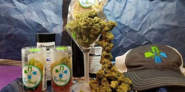 Cannabis products displayed with branded containers and a hat on a table.