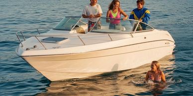Three people enjoy a boat ride while one swims nearby in calm water.
